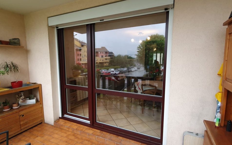 Vue extérieure terrasse couverte carrelée sur baie et porte vitrée